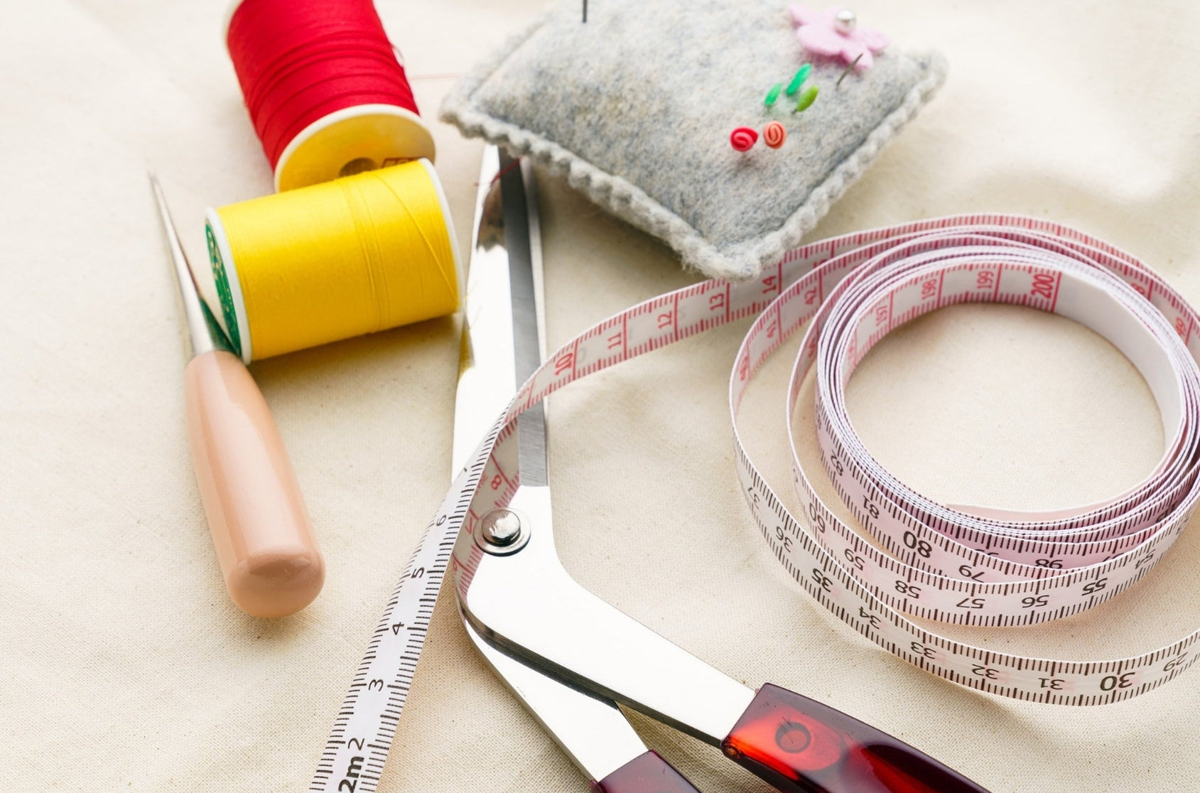 Sewing tools including scissors, thread, and a measuring tape on a light background